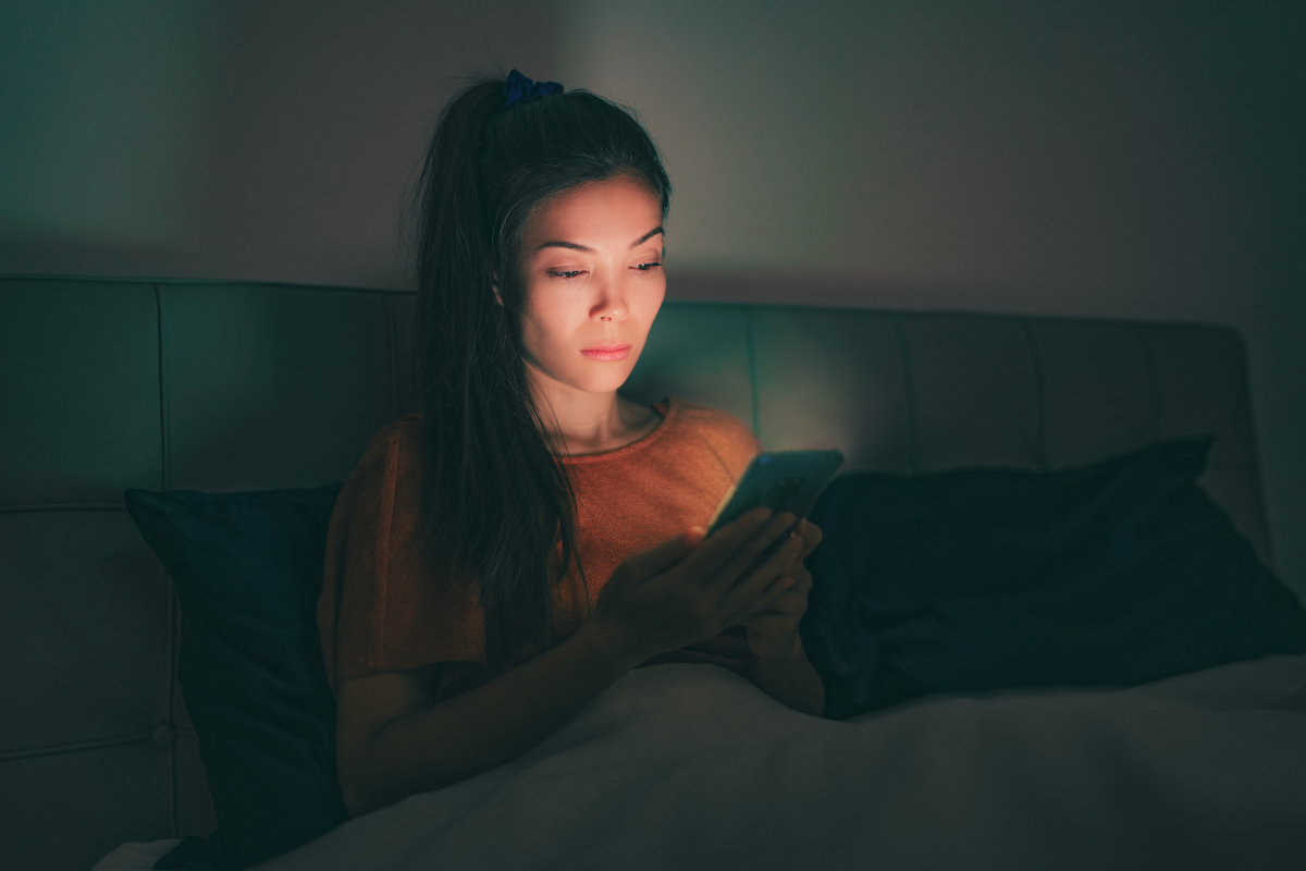 Woman sitting in a hotel bed on her phone in the middle of the night